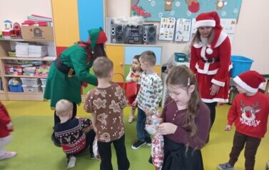 Elf i Pani Mikołajowa częstują dzieci cukierkami.