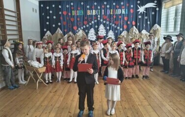 Uczniowie klasy II zapowiadają występ, w tle uczniowie klas I&ndash;III