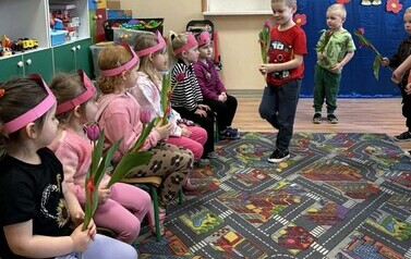 Chłopcy składają życzenia dziewczynkom i wręczają kwiaty.