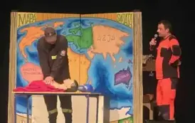 Ratownik medyczny wraz ze strażakiem uczą dzieci podstaw pierwszej pomocy przedmedycznej.
