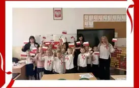 Grupowe zdjęcie dzieci z zajęć patriotycznych z kotylionami i flagami.