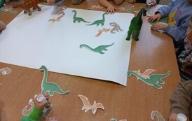 Dzieci tworzą wsp&oacute;lny plakat z dinozaurami.