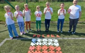 Wsp&oacute;lne zdjęcie uczni&oacute;w z kotylionami i z flagą zrobioną z puzzli